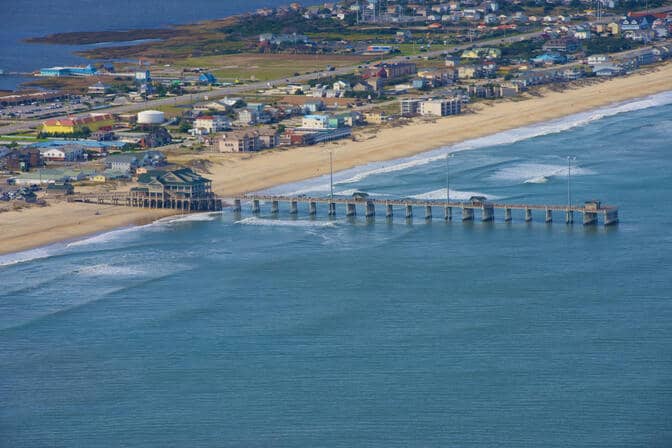 A long boardwalk extends into the vibrant blue waters of the Atlantic Ocean. A large structure is at the shore end of the pier.