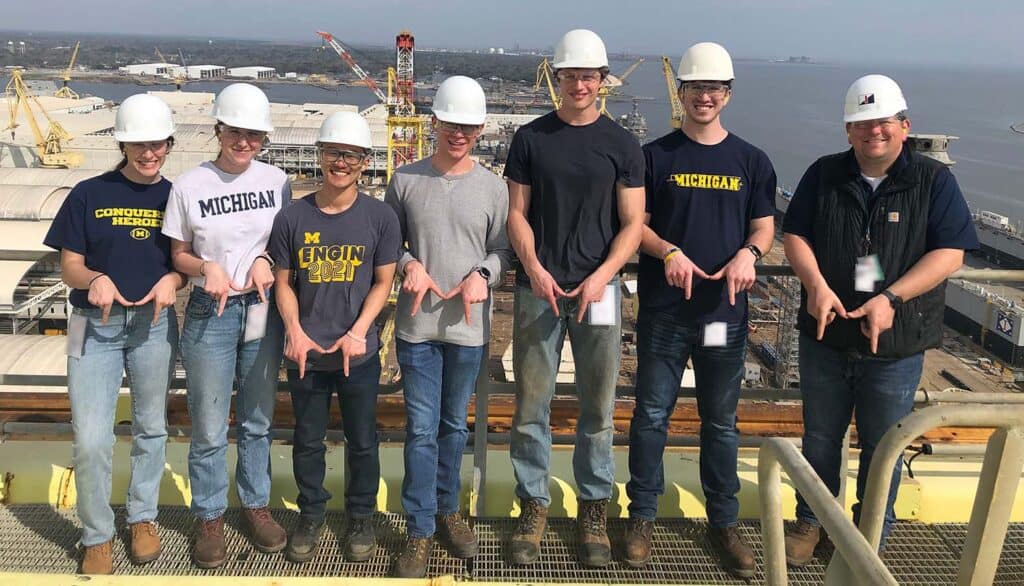 students on a large ship smiling at the camera making M sign with hands